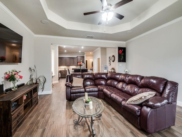 living area featuring visible vents, a tray ceiling, light wood-style floors, baseboards, and ceiling fan