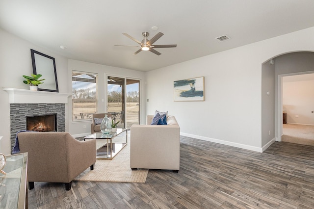 living area featuring a stone fireplace, wood finished floors, arched walkways, and baseboards