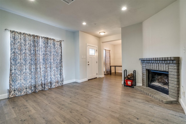 unfurnished living room featuring hardwood / wood-style flooring and a brick fireplace