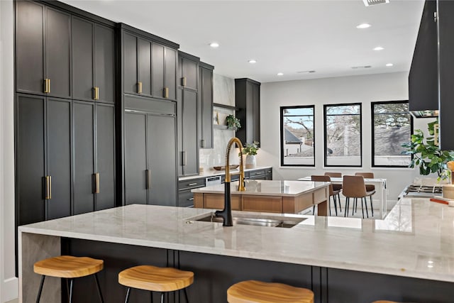 kitchen featuring recessed lighting, a sink, paneled refrigerator, and light stone countertops