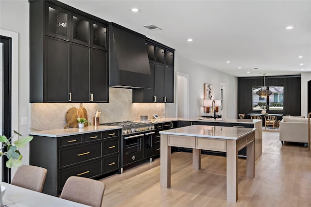 kitchen with wall chimney range hood, range with two ovens, a peninsula, dark cabinets, and recessed lighting