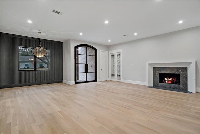 unfurnished living room featuring an inviting chandelier, french doors, a premium fireplace, and light wood-type flooring