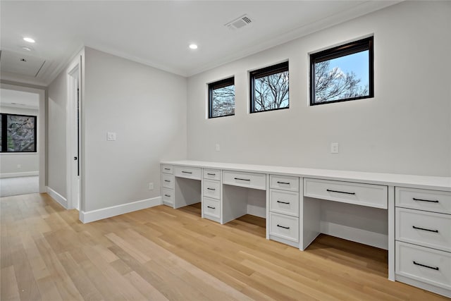 unfurnished office with light wood-type flooring, baseboards, built in desk, and visible vents