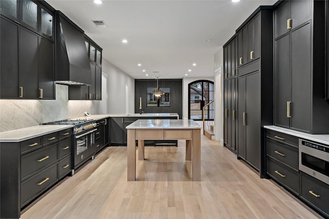 kitchen with pendant lighting, stainless steel microwave, tasteful backsplash, double oven range, and wall chimney exhaust hood