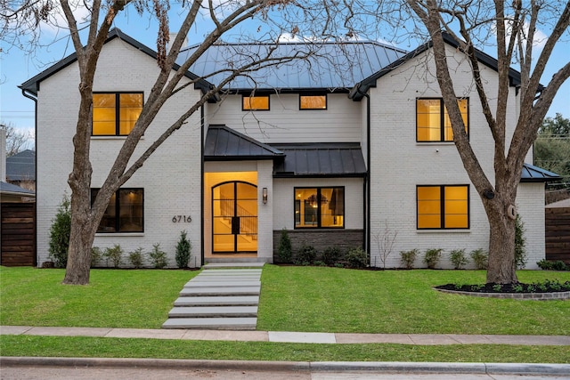 view of front of home featuring a standing seam roof, metal roof, a front lawn, and brick siding