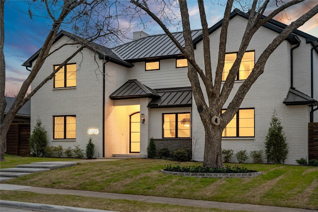 multi unit property featuring brick siding, metal roof, a front yard, and a standing seam roof