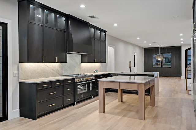 kitchen with pendant lighting, backsplash, light hardwood / wood-style floors, custom range hood, and range with two ovens