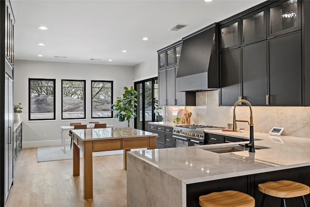 kitchen featuring wall chimney range hood, decorative backsplash, range with two ovens, a sink, and baseboards