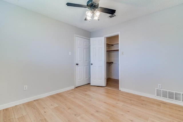 unfurnished bedroom with ceiling fan, a textured ceiling, a walk in closet, a closet, and light wood-type flooring