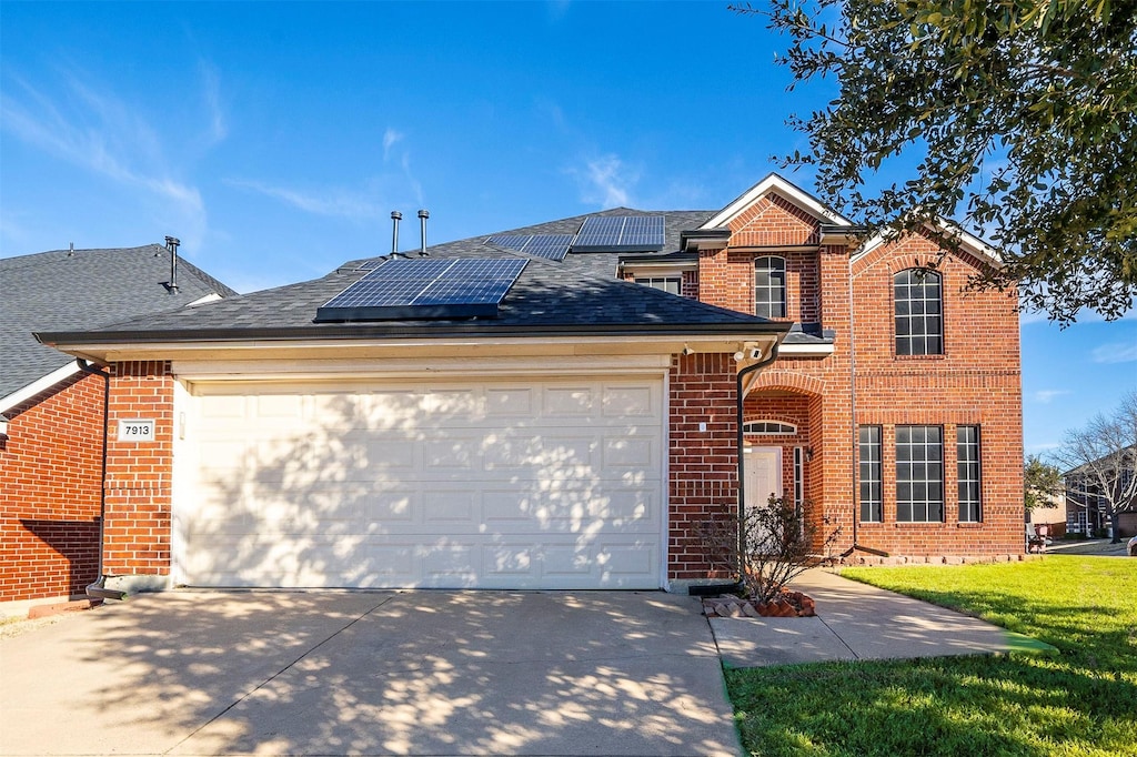 front facade featuring a garage, a front lawn, and solar panels