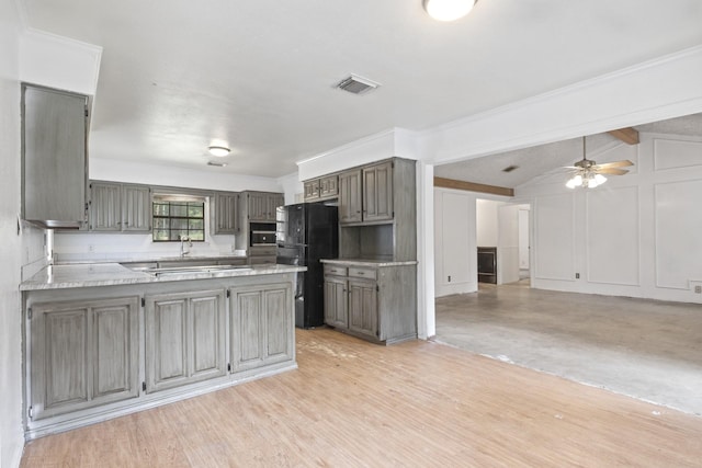 kitchen with vaulted ceiling with beams, ceiling fan, kitchen peninsula, black fridge, and light hardwood / wood-style flooring