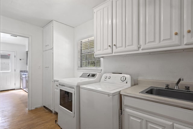 clothes washing area featuring sink, light hardwood / wood-style flooring, cabinets, and washing machine and clothes dryer