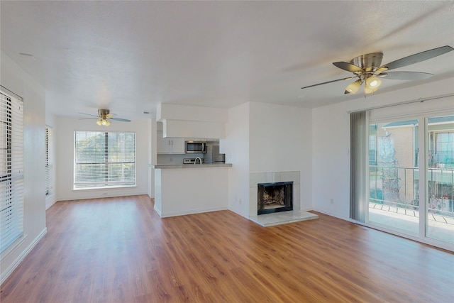 unfurnished living room with a tiled fireplace, light hardwood / wood-style floors, and ceiling fan