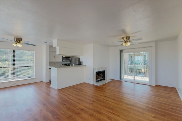 unfurnished living room with a tile fireplace, ceiling fan, and light wood-type flooring