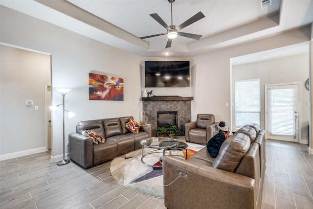 living room featuring a stone fireplace, a raised ceiling, and ceiling fan