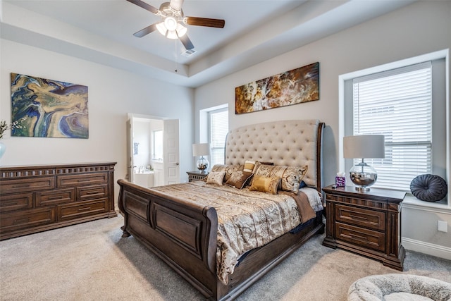 bedroom featuring a raised ceiling, light carpet, connected bathroom, and ceiling fan