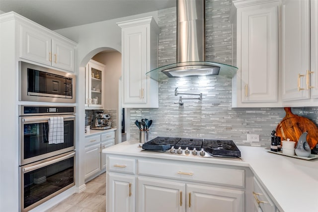 kitchen with stainless steel appliances, white cabinetry, light countertops, wall chimney range hood, and decorative backsplash