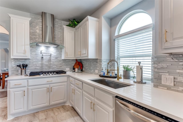 kitchen with white cabinets, appliances with stainless steel finishes, light countertops, wall chimney range hood, and a sink