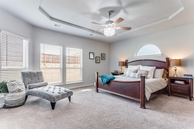 carpeted bedroom with a tray ceiling, visible vents, ceiling fan, and baseboards