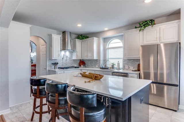 kitchen with arched walkways, a sink, white cabinets, wall chimney range hood, and appliances with stainless steel finishes