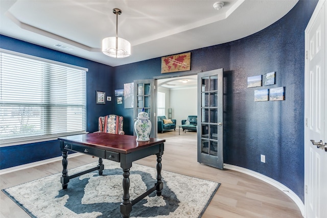 office with french doors, a raised ceiling, and light wood-type flooring