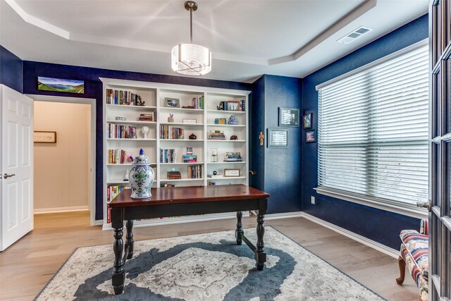 living room with crown molding, light hardwood / wood-style flooring, a tray ceiling, a notable chandelier, and a fireplace