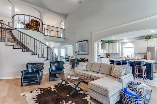 living room with arched walkways, stairway, a towering ceiling, light wood-style floors, and baseboards