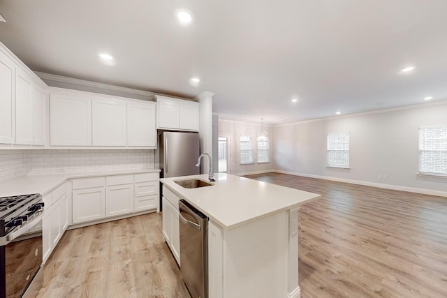 kitchen with appliances with stainless steel finishes, an island with sink, sink, white cabinets, and ornamental molding