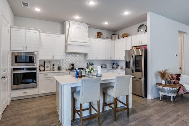 kitchen with white cabinetry, appliances with stainless steel finishes, custom range hood, and a kitchen breakfast bar