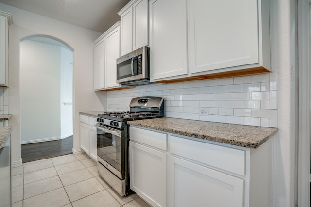 kitchen featuring stainless steel appliances, light stone countertops, white cabinets, and backsplash