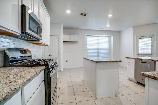 kitchen with appliances with stainless steel finishes, white cabinetry, backsplash, a center island, and light stone counters