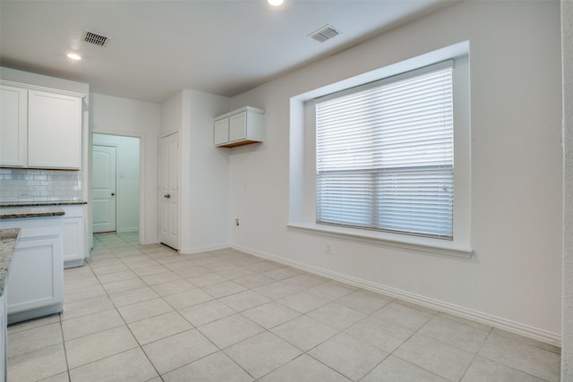 kitchen with white cabinetry, light tile patterned flooring, light stone counters, and decorative backsplash