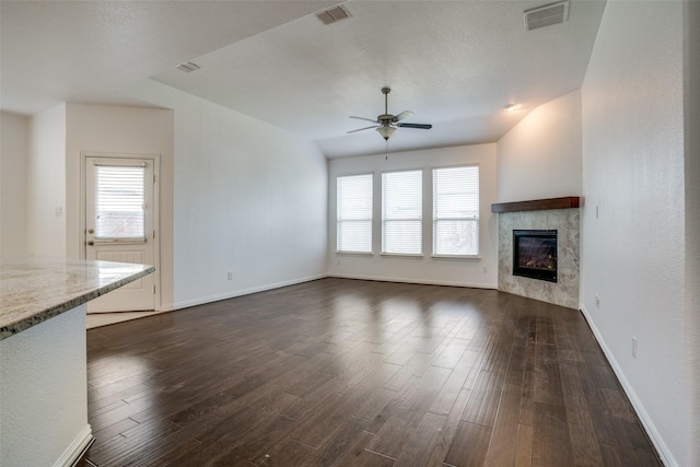 unfurnished living room featuring a tiled fireplace, dark hardwood / wood-style floors, and ceiling fan