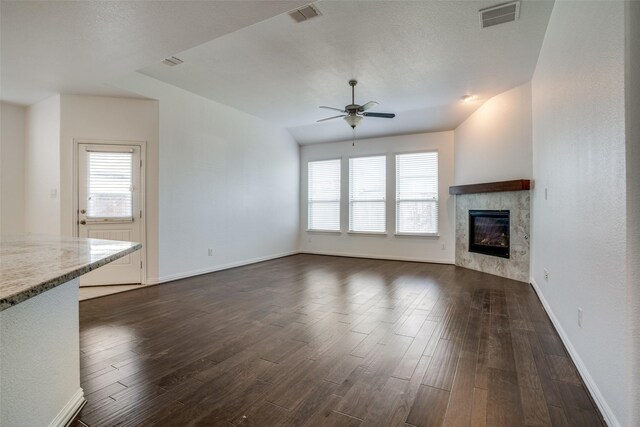 unfurnished living room with a tiled fireplace, ceiling fan, a wealth of natural light, and dark hardwood / wood-style flooring