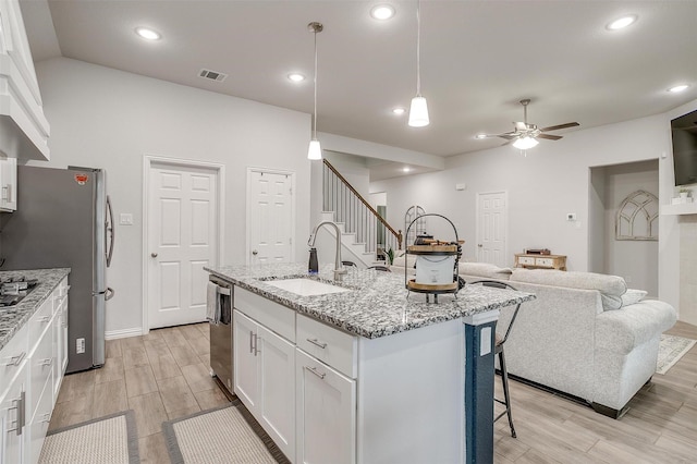 kitchen featuring sink, white cabinets, hanging light fixtures, light stone counters, and a center island with sink