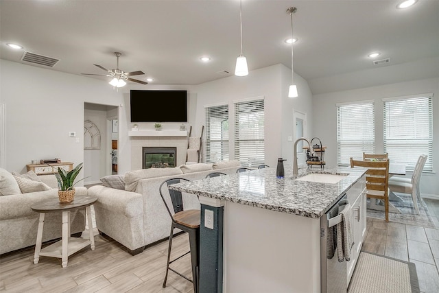 kitchen featuring sink, hanging light fixtures, stainless steel dishwasher, light stone countertops, and a kitchen island with sink