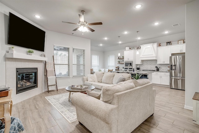 living room featuring a tiled fireplace, ceiling fan, and light hardwood / wood-style floors