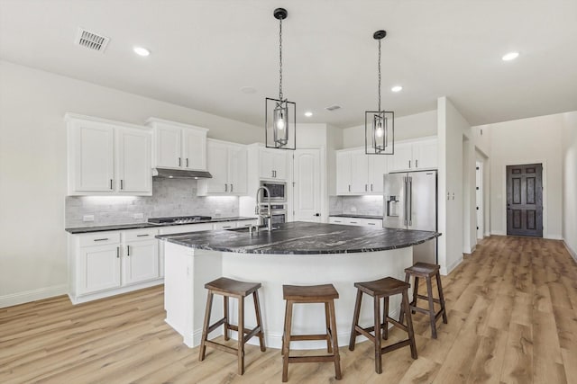 kitchen with appliances with stainless steel finishes, white cabinetry, sink, a breakfast bar area, and a center island with sink