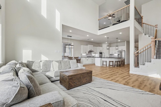 living room with a high ceiling, sink, a chandelier, and light hardwood / wood-style flooring