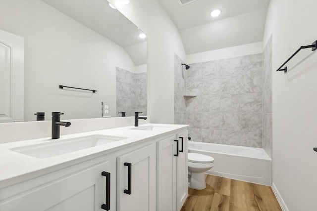 full bathroom featuring hardwood / wood-style flooring, tiled shower / bath combo, vanity, vaulted ceiling, and toilet