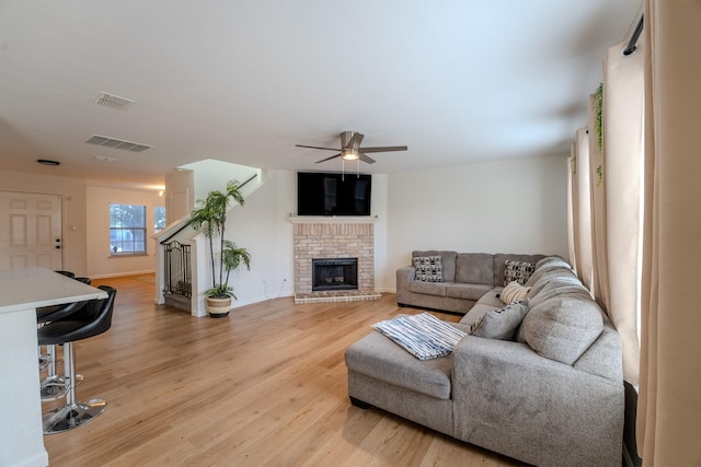 living room featuring ceiling fan, a brick fireplace, and light hardwood / wood-style floors