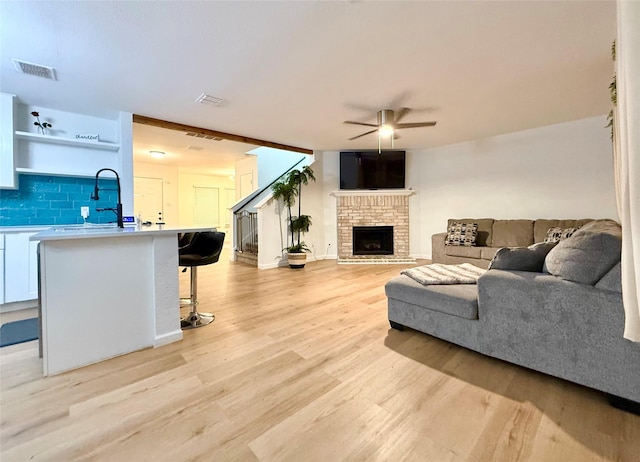 living room with ceiling fan, a brick fireplace, sink, and light hardwood / wood-style floors