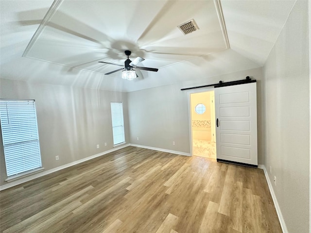 spare room with vaulted ceiling, a barn door, ceiling fan, and light hardwood / wood-style flooring