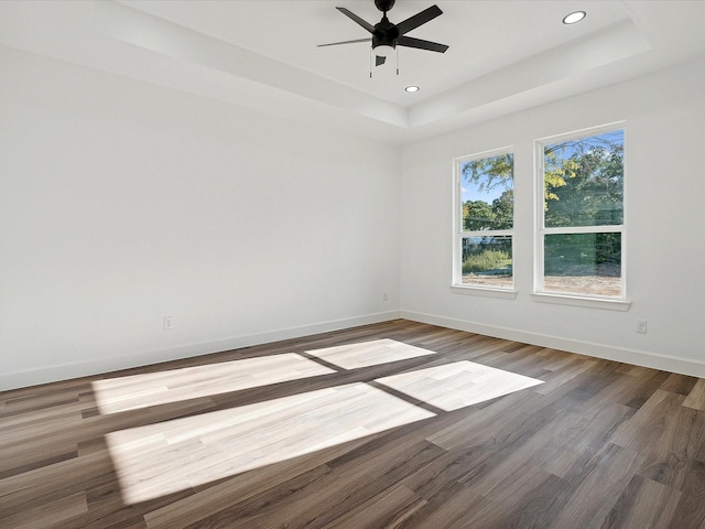 empty room featuring a raised ceiling, hardwood / wood-style flooring, and ceiling fan