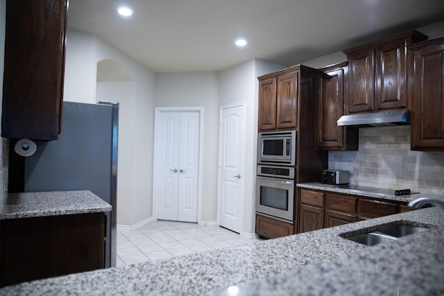 kitchen featuring dark brown cabinetry, sink, tasteful backsplash, light tile patterned floors, and appliances with stainless steel finishes