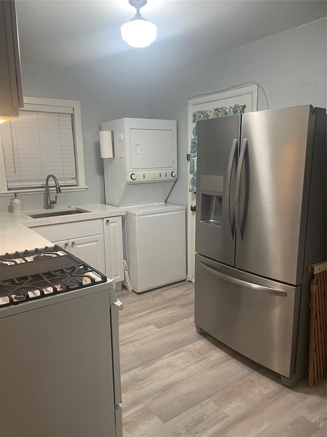 kitchen with sink, gas range gas stove, stacked washing maching and dryer, white cabinetry, and stainless steel fridge with ice dispenser