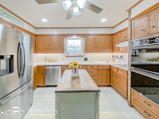 kitchen with appliances with stainless steel finishes, tasteful backsplash, ornamental molding, a textured ceiling, and a kitchen island