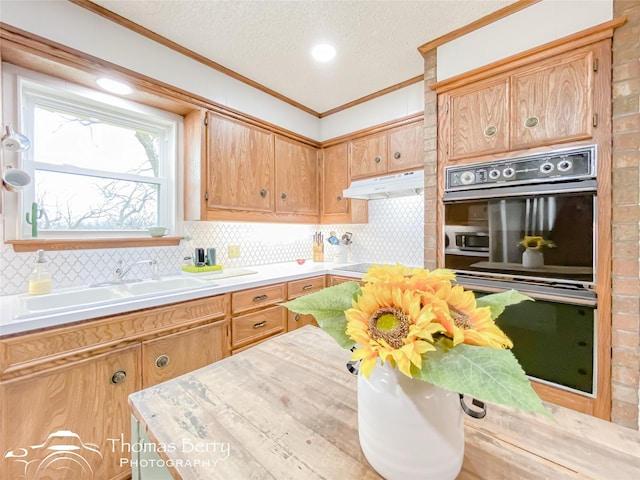 kitchen with sink, multiple ovens, black electric cooktop, ornamental molding, and backsplash