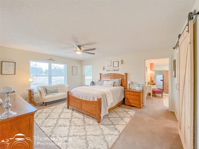 bedroom featuring a barn door, light colored carpet, a textured ceiling, and ceiling fan