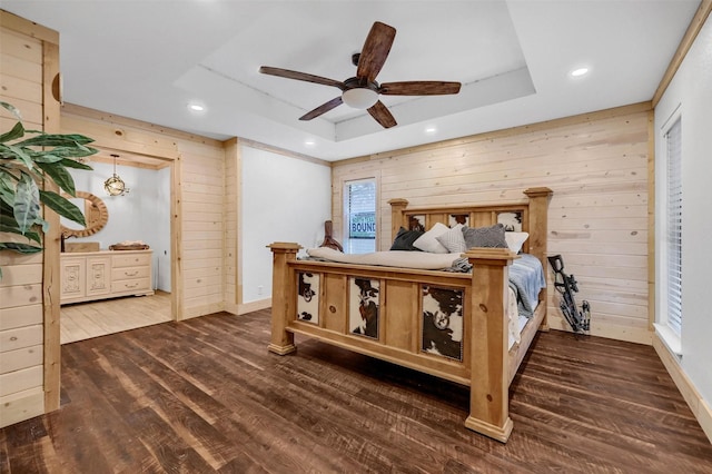 bedroom with a raised ceiling, dark hardwood / wood-style flooring, ceiling fan, and wood walls